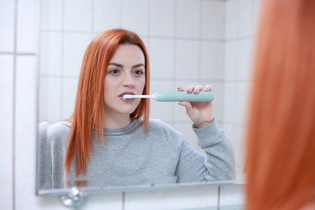 En rådhåret kvinde børster sine tænder med en eltandbørste